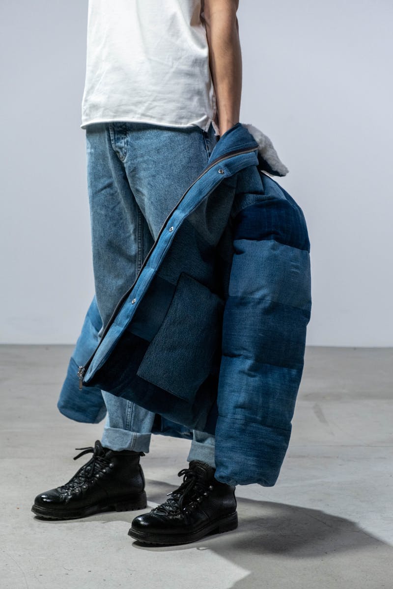 Man wearing blue jeans holding a stylish blue jacket, showcasing casual fashion.
